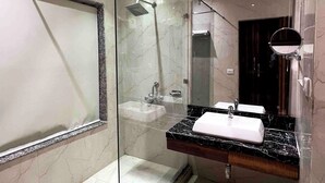 A modern bathroom with a glass-enclosed shower, a vanity with a marble countertop, and a large mirror. - Shoba Residency  (New Delhi)