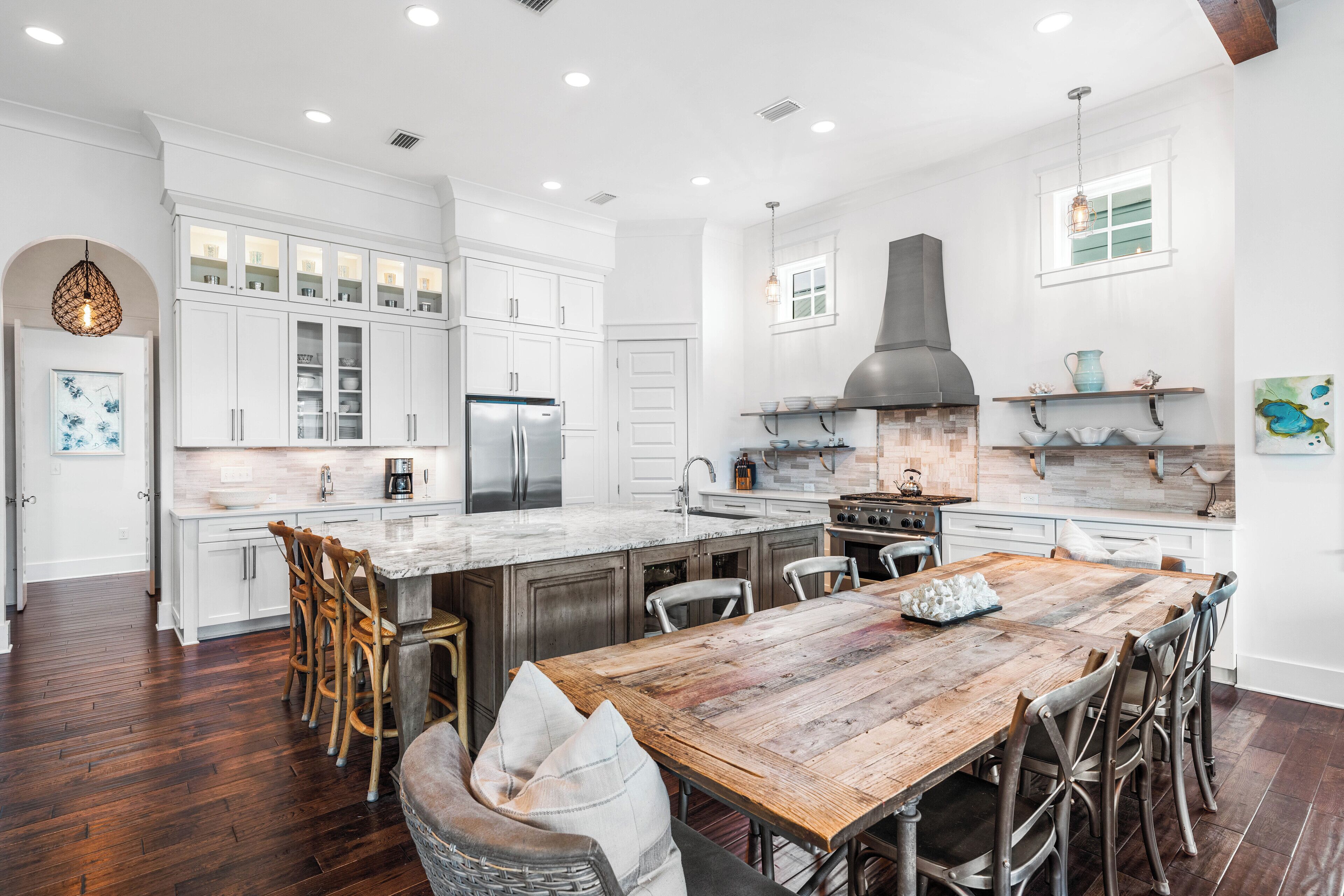 A spacious kitchen with white cabinetry, a large island, and a rustic dining table.