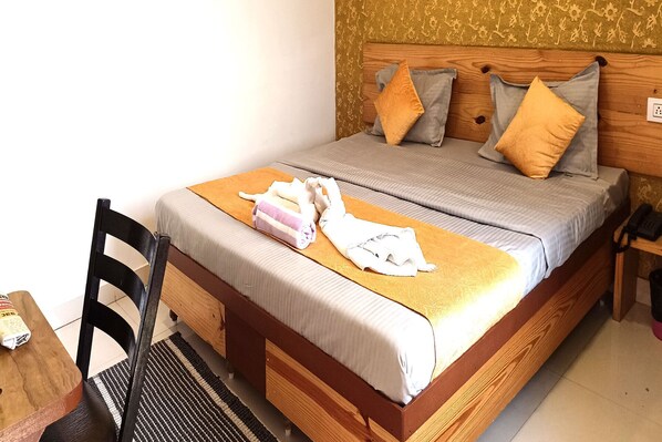 Una cama bien hecha con cabecera de madera, una silla negra y una mesita de noche con un teléfono.