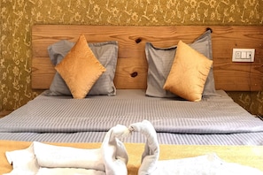 A bed with two pillows, a wooden headboard, and a power outlet on the wall.