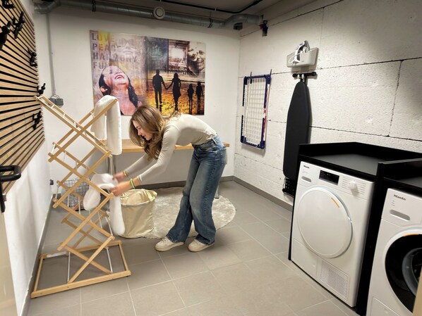 A laundry area with a washing machine, a drying rack, and a poster on the wall.