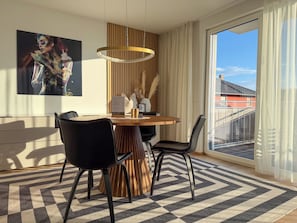 Een moderne eetruimte met een ronde tafel, zwarte stoelen, een houten accentmuur, een groot raam met uitzicht en een schilderij aan de muur.