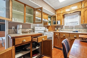 A compact kitchen with wooden cabinets, a microwave, a stove, and a dining area with a chair.