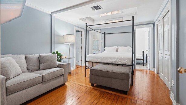 Ein Schlafzimmer mit Himmelbett, grauem Sofa und Holzboden.