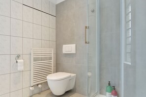 A modern bathroom with a toilet, a glass shower enclosure, and a towel rack.