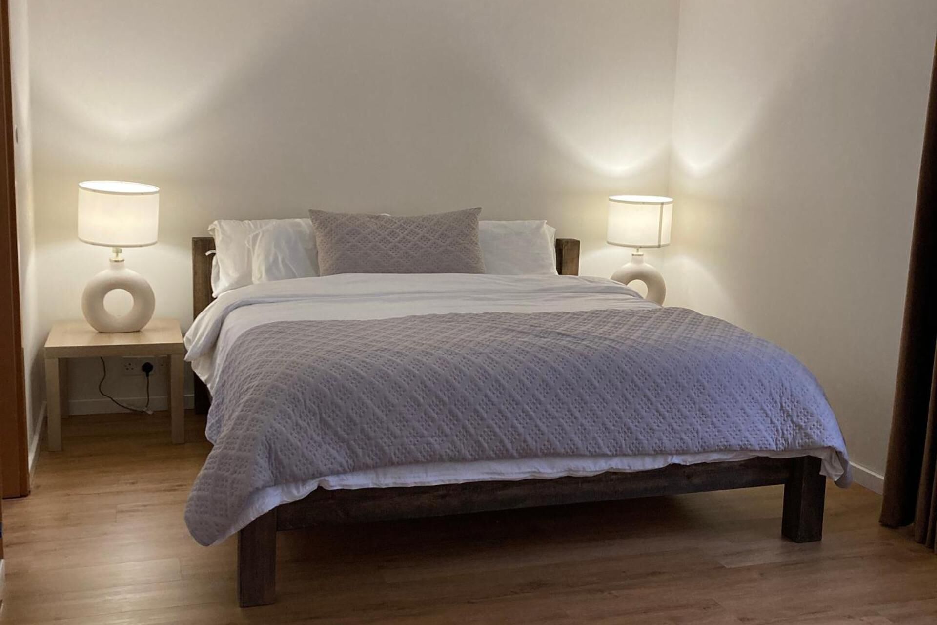 A bedroom with a wooden bed, white bedding, two bedside lamps, and a nightstand.