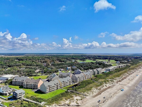 A coastal hotel with multiple buildings, a beach, and a golf course in the background.
