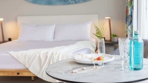 A neatly made bed with white linens, a bedside table with a water bottle and a glass, and a wall with a blue abstract painting. - Waikiki studio w/ pool, sauna & city views (Honolulu)
