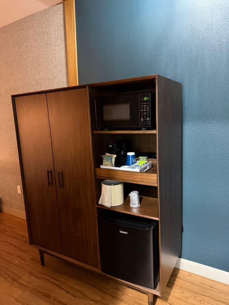 Eine Küchenzeile mit einer Mikrowelle, einem kleinen Kühlschrank und einem Schrank mit Regalen.