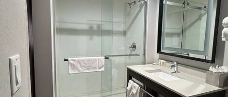 Un baño moderno con cabina de ducha de vidrio, tocador con espejo y suelo de baldosas.