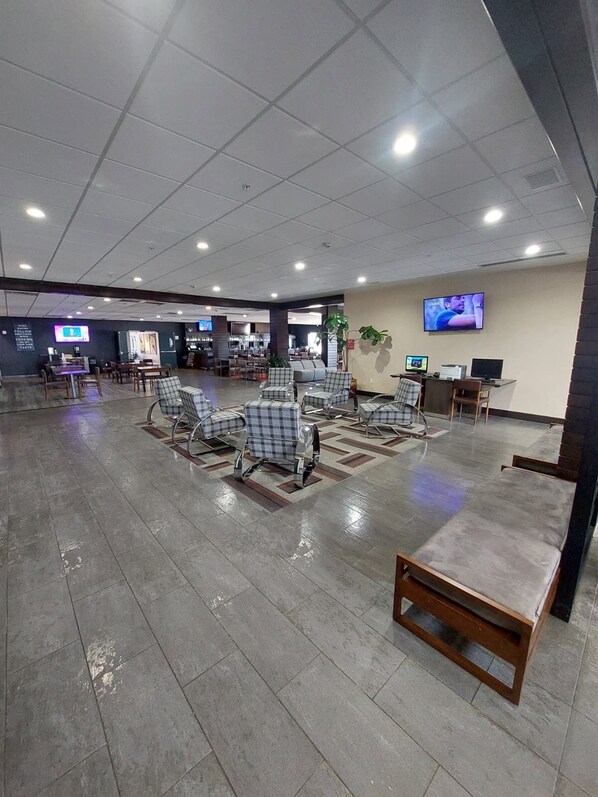 Um espaço amplo e interno com piso revestido, vários conjuntos de assentos e uma televisão na parede.