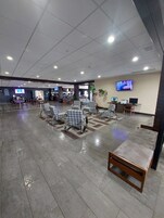 A spacious indoor area with tiled flooring, multiple seating arrangements, and a television mounted on the wall.
