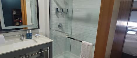 Un baño moderno con ducha de vidrio, tocador con espejo y barra para toallas.