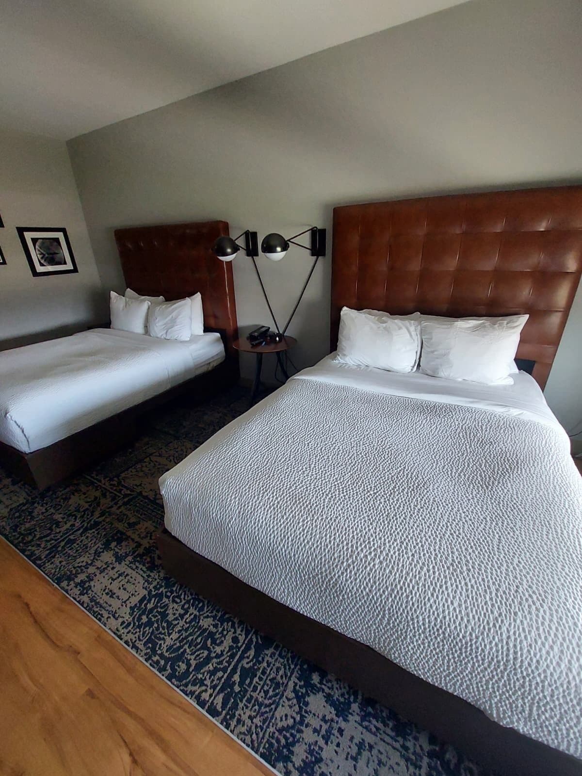 A hotel room with two single beds and one double bed, a small round table with a lamp, and a patterned rug.