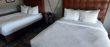 A hotel room with two single beds and one double bed, a small round table with a lamp, and a patterned rug.