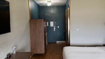 A hotel room with a bed, desk, wardrobe, and a door leading to another room.