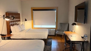 Habitación de hotel con dos camas, un escritorio, una silla, un ventanal grande y una lámpara en el techo.