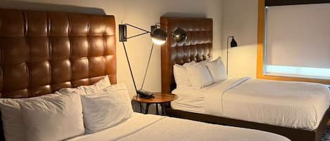 Una habitación de hotel con dos camas, un ventanal grande, un cabecero y una lámpara de pie.