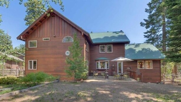 A two-story wooden cabin with a covered patio area and a fenced yard.