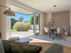 Ein modernes Wohnzimmer mit einer Couch, einem Esstisch mit Stühlen und einer großen Glasschiebetür, die auf eine Terrasse führt.
