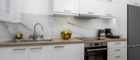 Una cocina moderna con armarios blancos, un refrigerador de acero inoxidable, un horno empotrado y una encimera de madera.