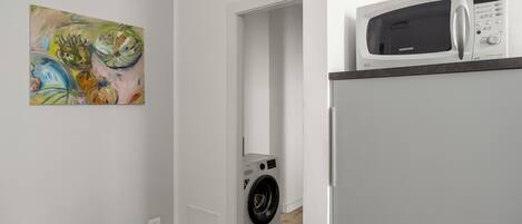 A laundry room with a washing machine and a microwave on a counter.