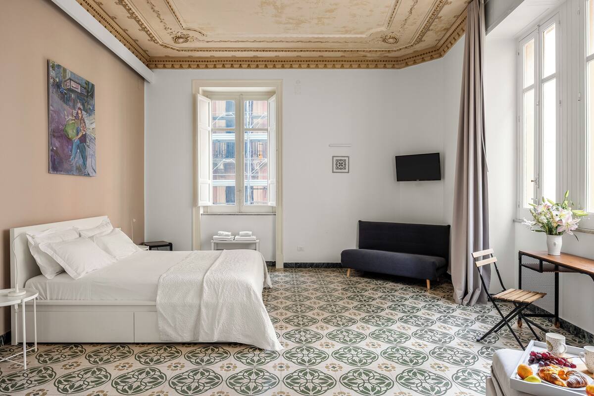 A hotel room with a bed, a desk with a chair, a television, and a breakfast tray.