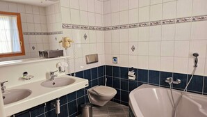 A bathroom with two sinks, a toilet, and a bathtub with a showerhead. - Hôtel Restaurant Le Cavalier (Soyhières)