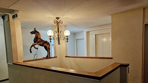 A reception desk with a horse sculpture, a chandelier, and a mirror reflecting a door. - Hôtel Restaurant Le Cavalier (Soyhières)