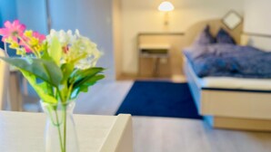A room with a bed, bedside table, lamp, and a vase with flowers. - Hôtel Restaurant Le Cavalier (Soyhières)