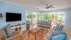 Ein Wohnzimmer mit Flachbildfernseher, Holzmöbeln und einer großen Schiebetür zu einer Außenpatio.