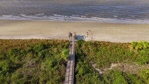 Una passerella in legno che conduce a una spiaggia con un litorale sabbioso e onde oceaniche.