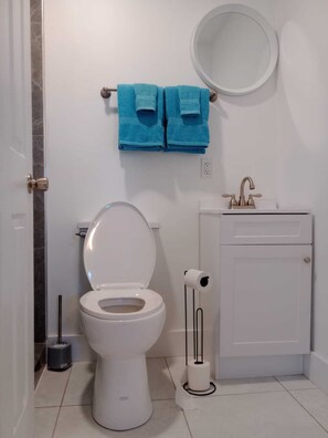 Ein modernes Badezimmer mit einer weißen Toilette, einem Waschbecken mit goldenem Wasserhahn und zwei blauen Handtüchern, die auf einem Handtuchhalter hängen.