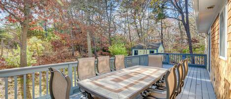 A wooden deck with a table and chairs, surrounded by trees with autumn foliage.