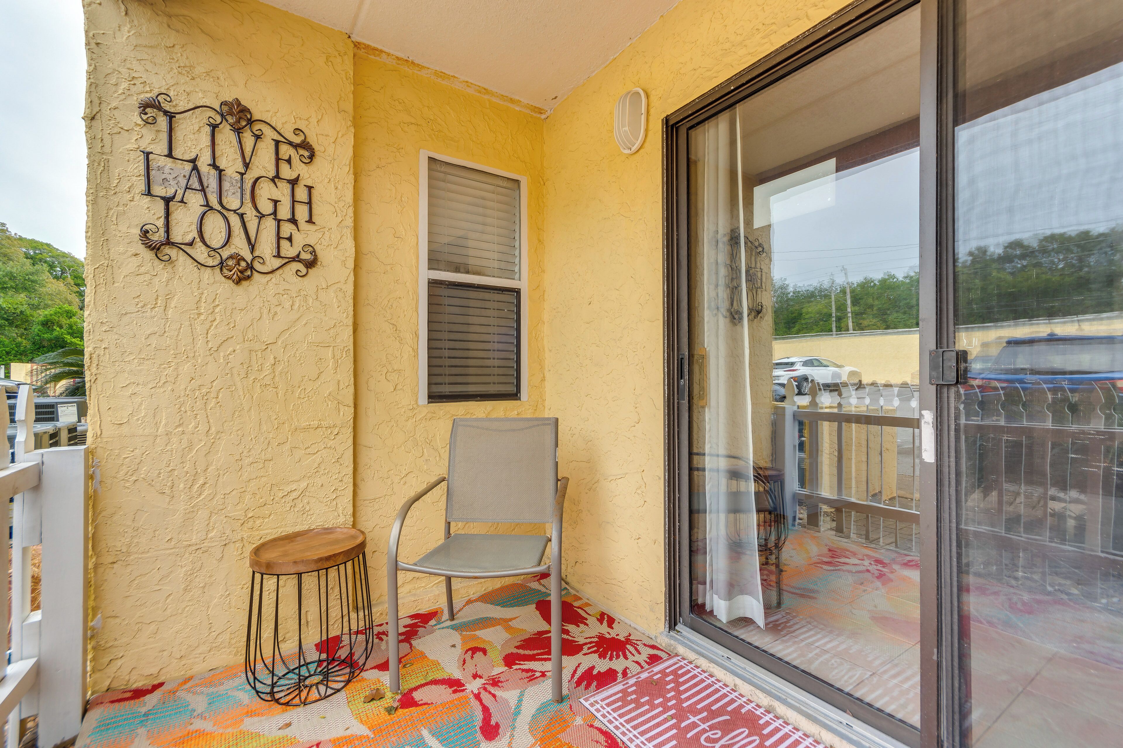 A balcony with a chair, a decorative sign, a window with blinds, and a glass door.