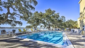 Piscina retangular com deck ladrilhado, rodeada por espreguiçadeiras e árvores.