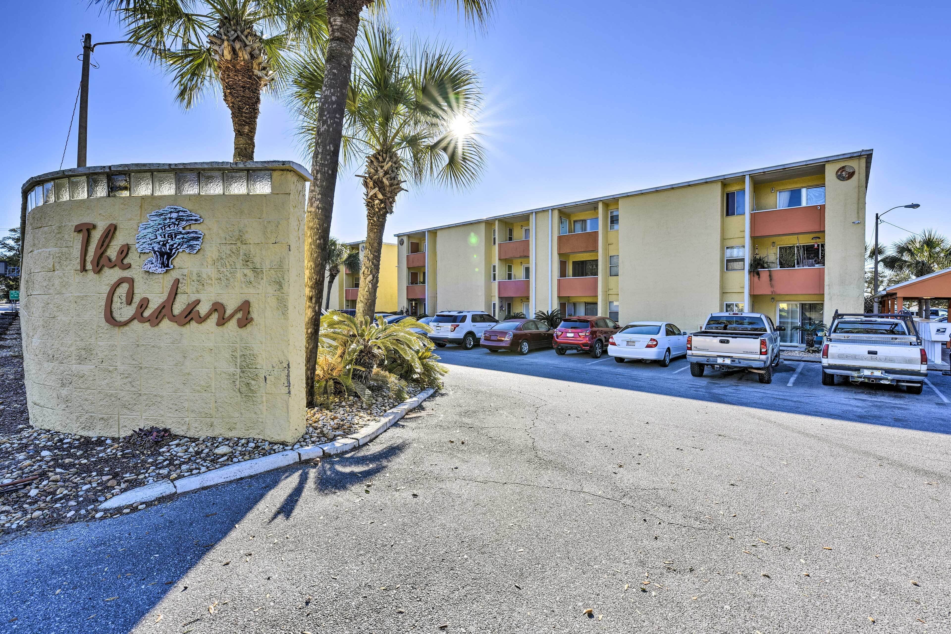 A building with a sign reading "The Cedars" and a parking lot with several cars.