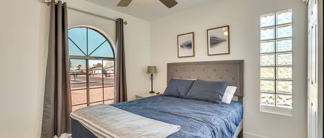 A bedroom with a bed, a ceiling fan, a window with curtains, and a nightstand with a lamp.