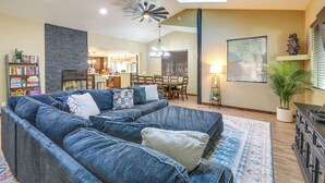 A modern living room with a sectional sofa, a fireplace, a dining area, and a kitchen in the background. - Gazebo w/ View & EV Charger: Rustic Williams Cabin (Williams)
