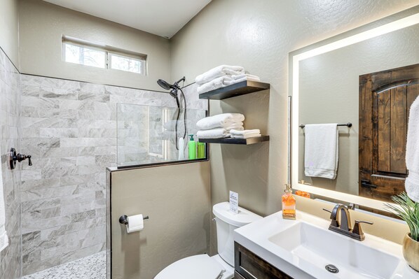A bathroom with a glass-enclosed shower, a white toilet, a sink with a mirror, and a towel rack. - Gazebo w/ View & EV Charger: Rustic Williams Cabin (Williams)