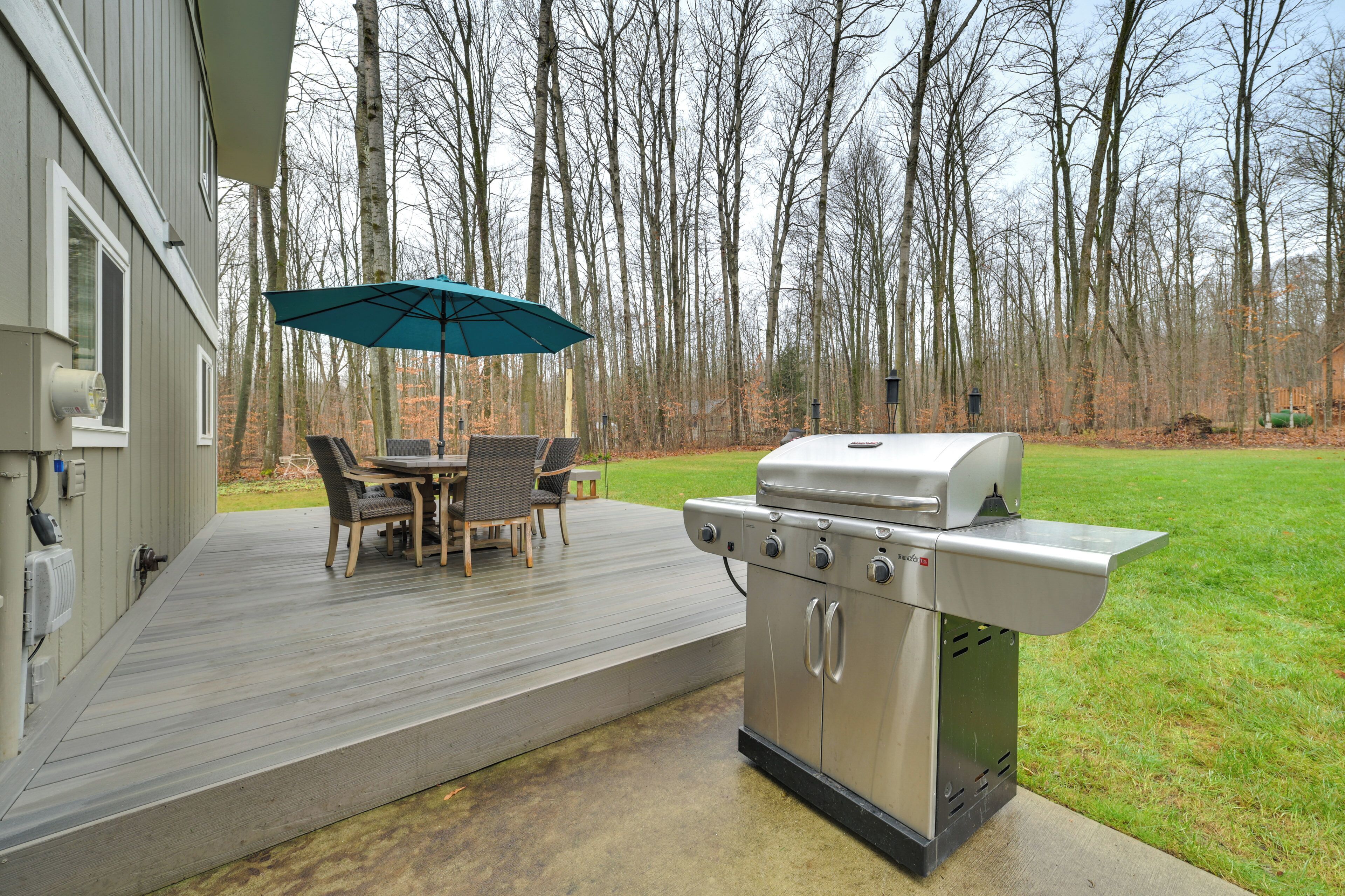 An outdoor deck with a grill, a table with chairs, and an umbrella.
