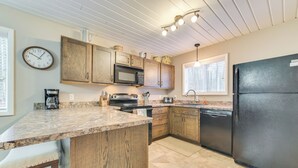 A kitchen with wooden cabinets, a black refrigerator, a microwave, a coffee maker, and a clock on the wall.