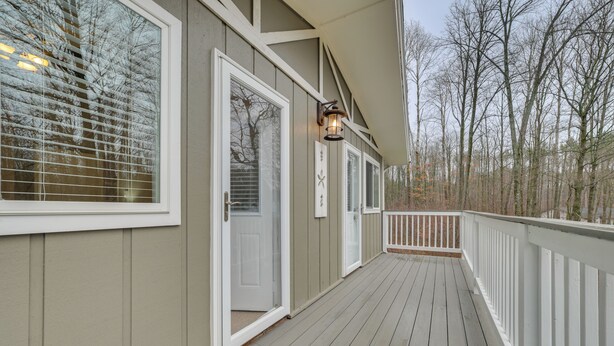 A wooden deck with white railings, a door, and a wall-mounted light fixture.