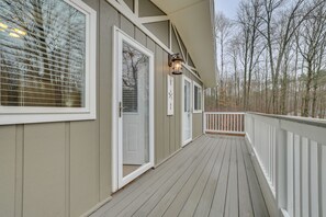 A wooden deck with white railings, a door, and a wall-mounted light fixture.