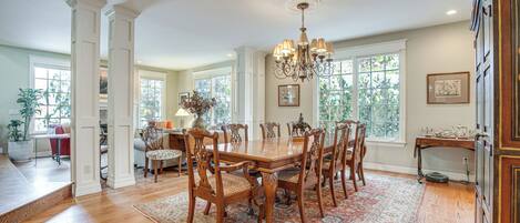 A spacious dining area with a large wooden table, surrounded by ornate chairs, set on a patterned rug.