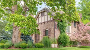A traditional brick house with a gabled roof, surrounded by a well-maintained garden with various shrubs and a large tree. - Walk to DU, Dining & Parks: Spacious Denver Home! (Denver)