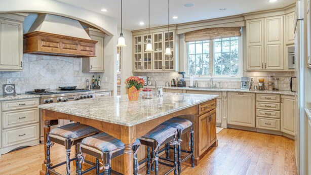 A spacious kitchen with a large island, wooden bar stools, and a window providing natural light. - Walk to DU, Dining & Parks: Spacious Denver Home! (Denver)