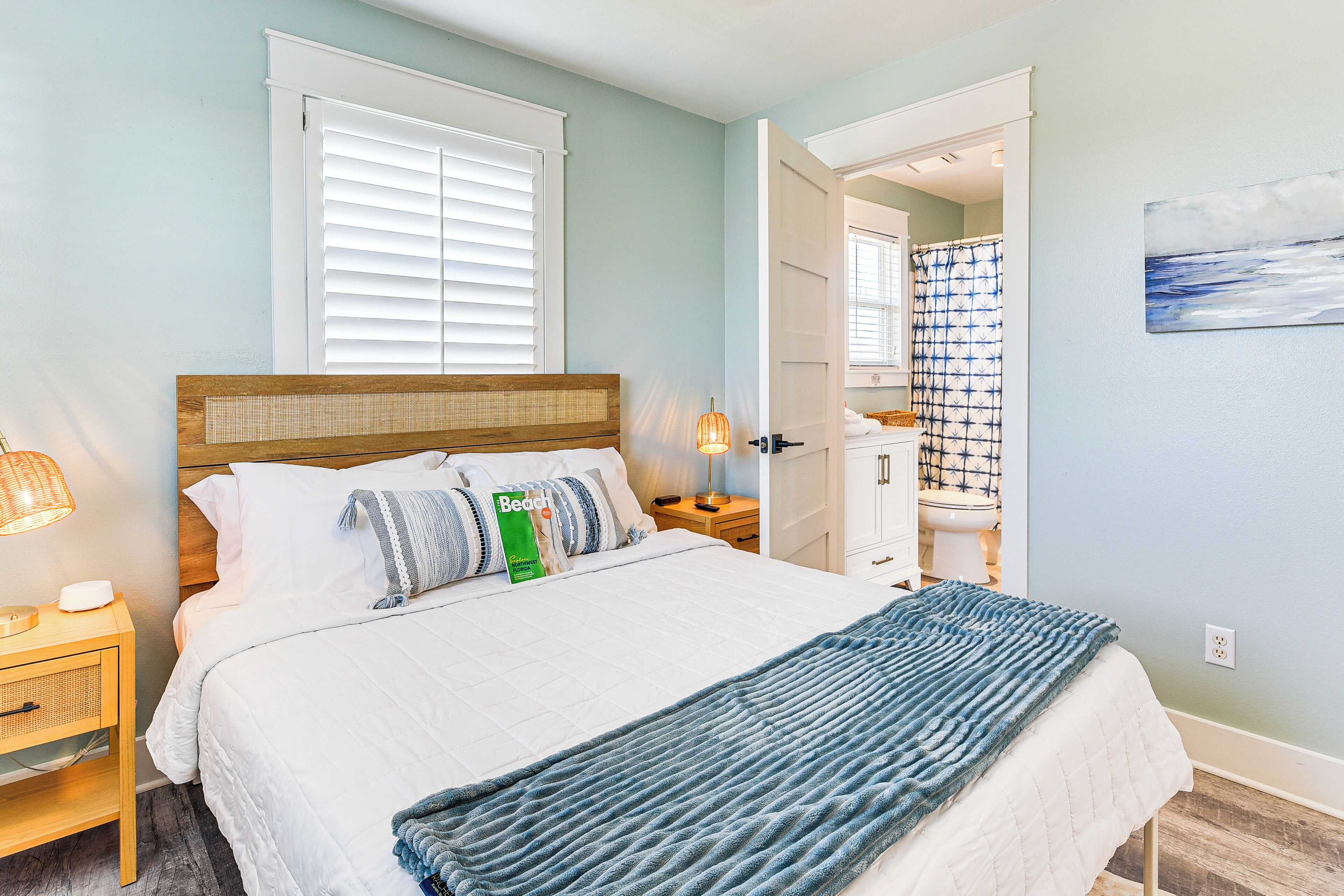 Un dormitorio con cama, mesita de noche, lámpara y vistas al baño.