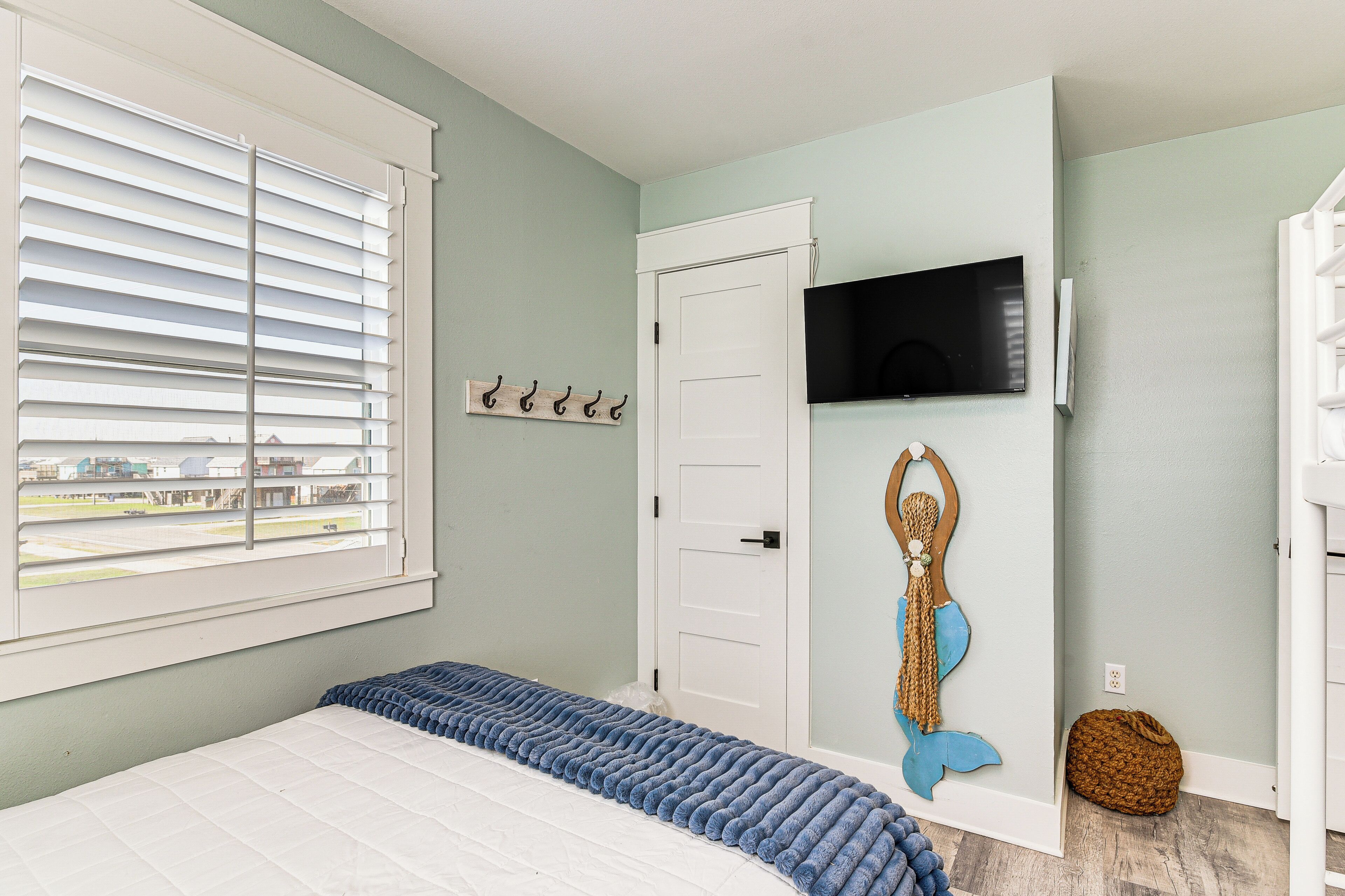 A bedroom with a bed, a window with blinds, a door, a mounted TV, and a wall decoration.