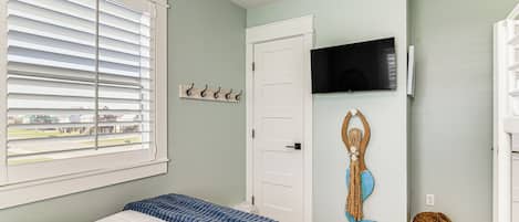 A bedroom with a bed, a window with blinds, a door, a mounted TV, and a wall decoration.